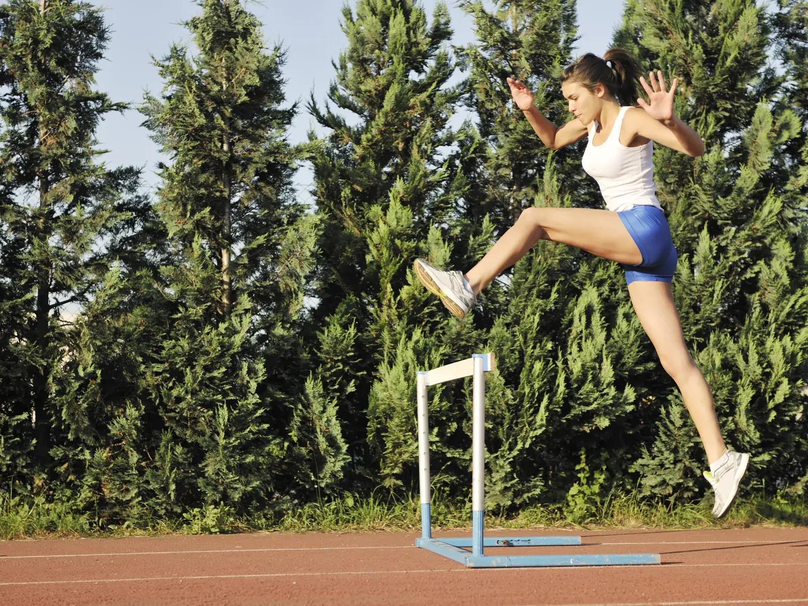 A teenage athlete clearing a hurdle on a track