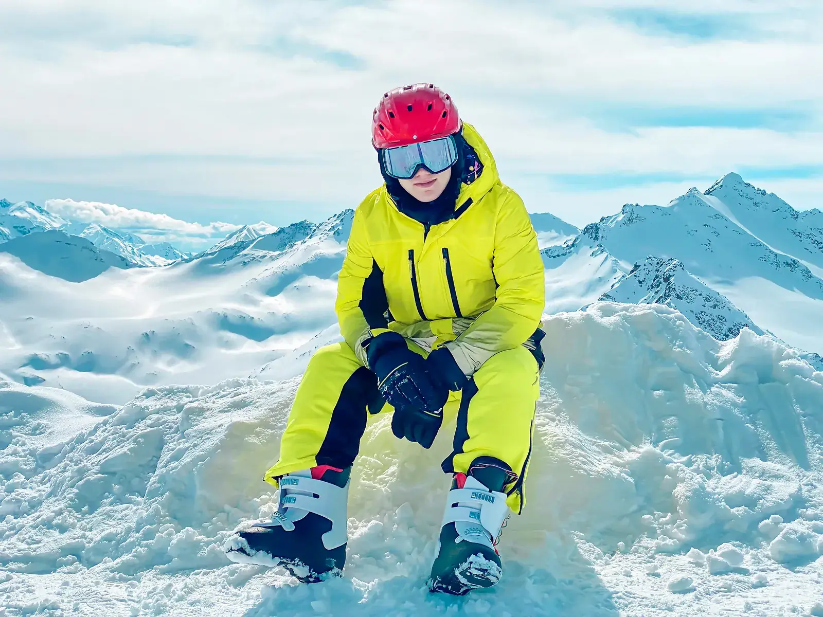 A child in a snowsuit and helmet sitting on a snowy mountain