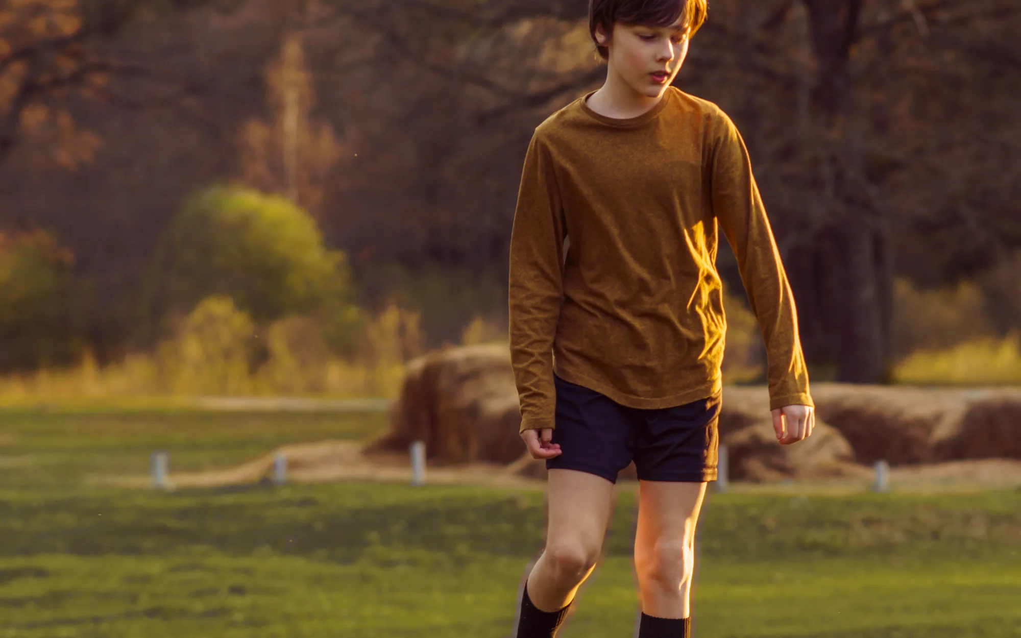 A teenage soccer player on a field at golden hour