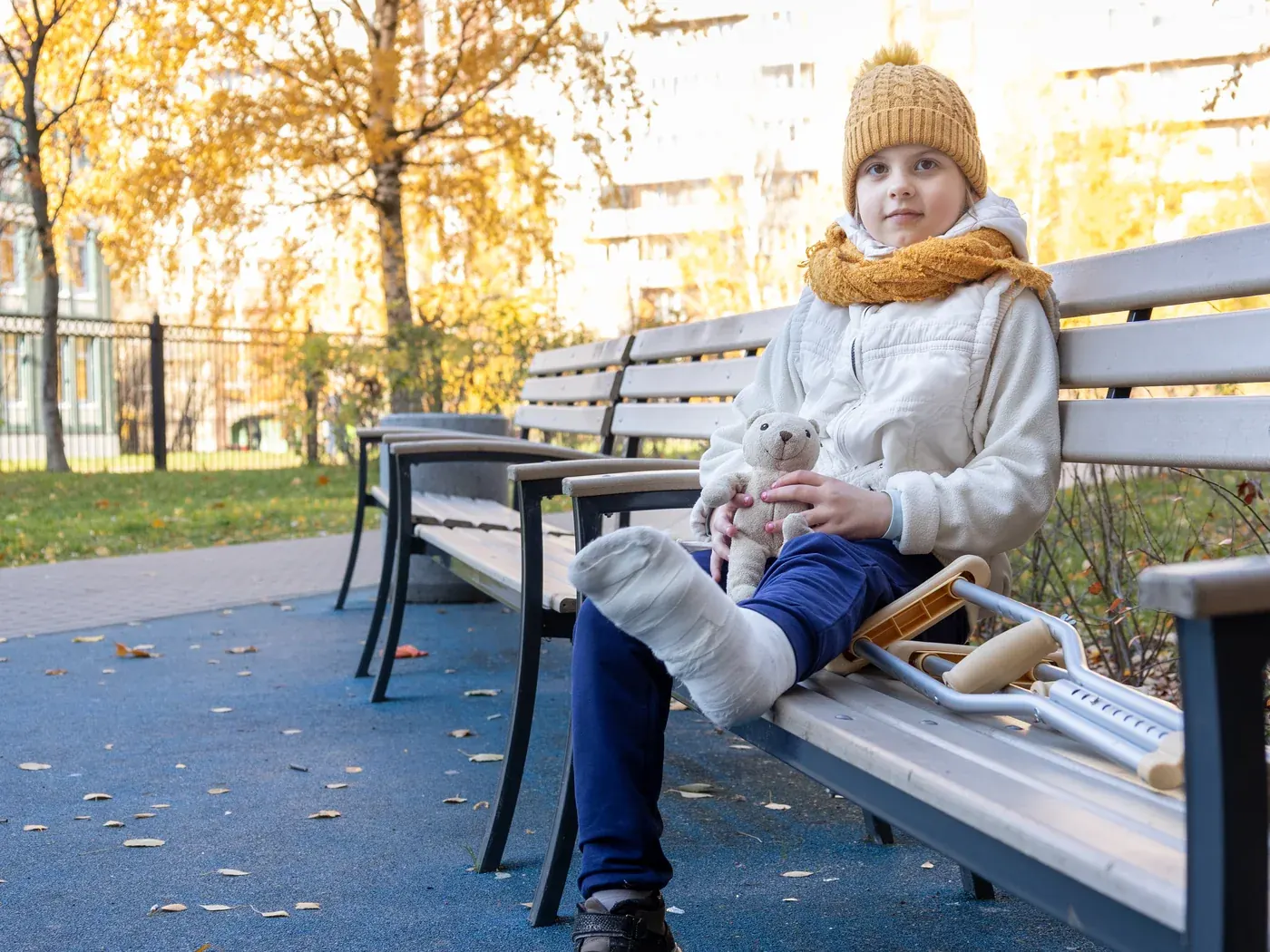 A child with a leg cast and crutches resting on a park bench